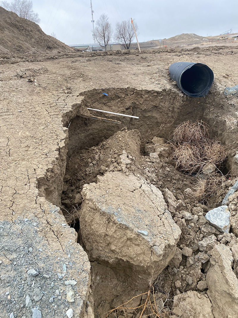 A section of eroded earth with large cracks and a partially collapsed pipe on barren land. Dry vegetation is visible in the crevices. A section of eroded earth with large cracks and a partially collapsed pipe on barren land. Dry vegetation is visible in the crevices.