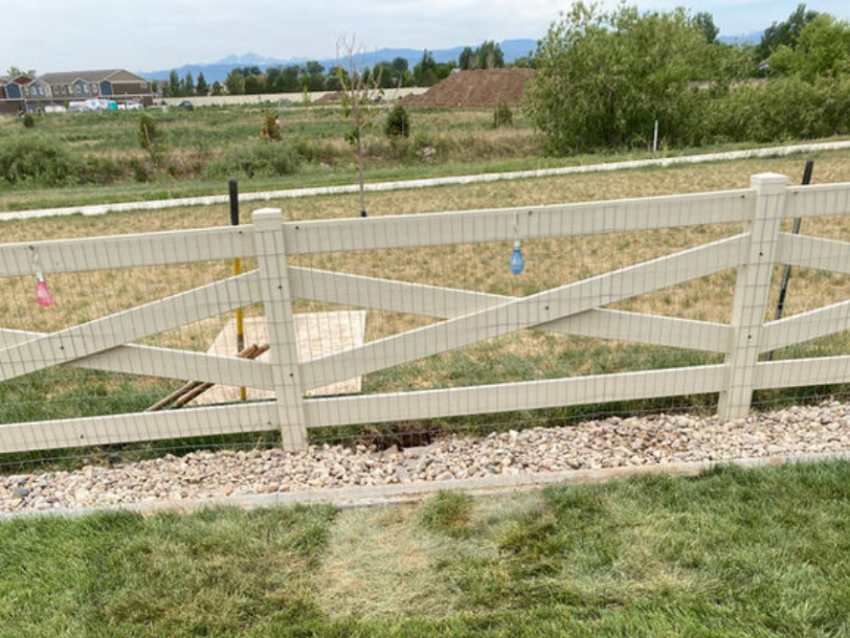 Wooden fence in a grassy yard, with a pathway and small decorative lights hanging on the fence. Trees and mountains are visible in the distance.