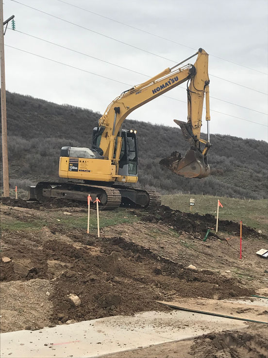 Yellow excavator digging earth on a hillside construction site, surrounded by dirt and scattered markers.